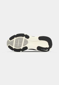 Semelle d’une chaussure de sport noire et blanche avec des sections en caoutchouc noir texturé et des zones rembourrées grises pour l’adhérence et le soutien.