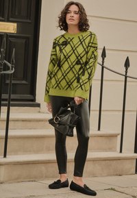 Green argyle sweater, black faux leather leggings, black loafers, and a small black bag with a circular handle, on outdoor steps.
