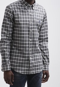 Camisa de botones en cuadros azul marino y verde, fabricada en algodón, de mangas largas y con logo en el pecho izquierdo. Presenta botones frontales y un cuello desplegado.