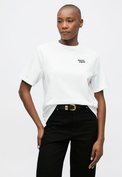 Tricou alb din bumbac, cu mâneci scurte, având brodat în negru textul "Maison Kitsuné." Asortat cu pantaloni negri și o curea cu cataramă aurie.