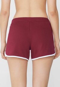 Shorts bordeaux avec une texture douce, présentant un liseré blanc le long de l'ourlet et de la taille. Conçus pour le confort et la liberté de mouvement.