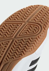 Suela de goma marrón con patrón de tracción en zigzag; parte superior blanca con franjas negras en contraste; textura suave, bordes redondeados.