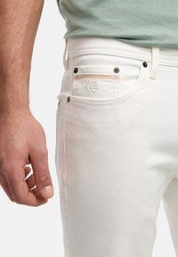 Białe dżinsy bawełniane o slim fit, pięciopocketowym kroju, czarnych metalowych akcentach i subtelnych pomarańczowych przeszyciach na tylnej kieszeni.