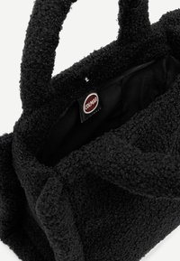 Melnas strukturētas rokas somas ar mīkstu, pūkainu virsmu. Iekšpusē ir vienota melna oderēšana un redzama zīmola birka ar uzrakstu "COLMAR."