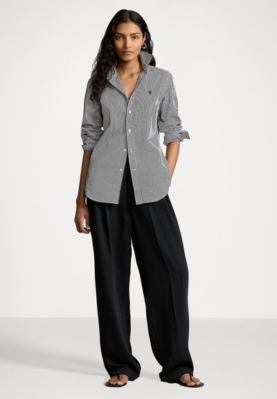 Chemise à rayures en noir et blanc, avec un grand col, un corsage cintré et des manches retroussées. Associée à un pantalon noir ample.