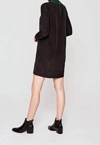 Svart långärmad klänning med rund halsringning, har en grön detalj på baksidan och en fåll som når mitt på låret. Matchad med svarta ankelstövlar.