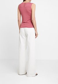 Ärmlös rosa topp med rund halsringning och nyckelhål på baksidan, i kombination med vita vida byxor, visad bakifrån.