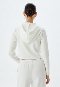 Witte cropped hoodie met een zachte, gladde textuur en een capuchon, gecombineerd met bijpassende broek met elastische taille. Eenvoudig en minimaal ontwerp.