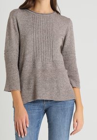 Ljusbrun stickad tröja med en texturerad kropp, ribbade detaljer och 3/4-långa ärmar. Matchad med denimjeans.