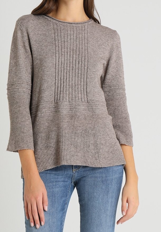Ljusbrun stickad tröja med en texturerad kropp, ribbade detaljer och 3/4-långa ärmar. Matchad med denimjeans.