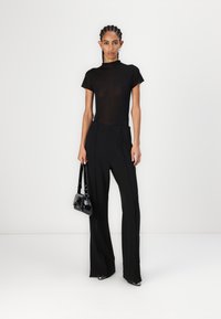 Černý slim-fit top s krátkými rukávy se kombinujte s černými volnými kalhotami s vysokým pasem. Modelka drží malou černou kabelku.