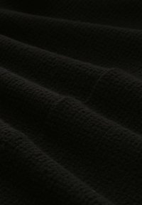 Tissu noir texturé avec un motif gaufré, drapé et présentant des plis doux et de la profondeur, avec une finition mate.