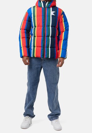 Chaqueta acolchada con rayas en rojo, azul, verde y amarillo, con capucha y cremallera frontal; combinada con vaqueros azul claro y zapatillas blancas.