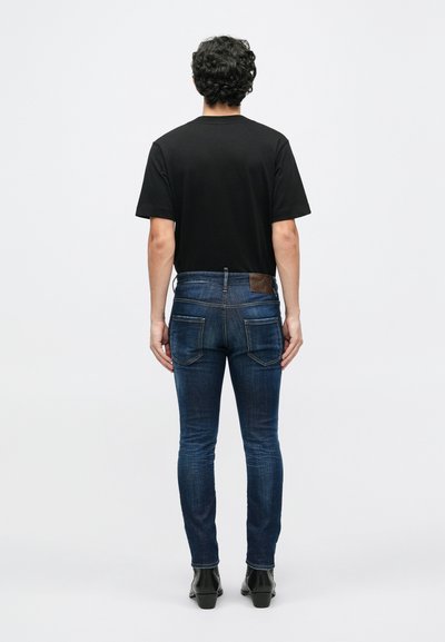 Camiseta negra de manga corta combinada con jeans ajustados azules, que cuentan con bolsillos traseros y una etiqueta de cuero en la cintura. Botines negros.