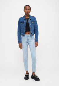 Denim jakna temno modre barve z gumbi, v kombinaciji s črnim kratkim topom in svetlo modrimi skinny jeans hlačami. Črne platforme z verižnimi detajli.