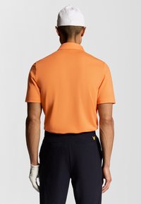 Orange polo shirt med korte ærmer, glat tekstur og spids krave, parret med mørke bukser med et lille gult logo.