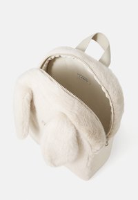 Faux fur cream backpack with soft, rounded shape, zip closure, and two floppy ears. Adjustable fabric strap on top and inner tag visible.