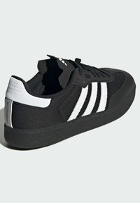 Czarne buty sportowe z białymi paskami, tkaninowa cholewka, gumowa podeszwa i okrągły czubek. Posiadają sznurowane zapięcie oraz fakturowane akcenty na pięcie.