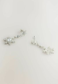 Pendientes en tono plata con diseños de copos de nieve, adornados con diversas piedras preciosas transparentes, que muestran una combinación de superficies lisas y texturizadas.