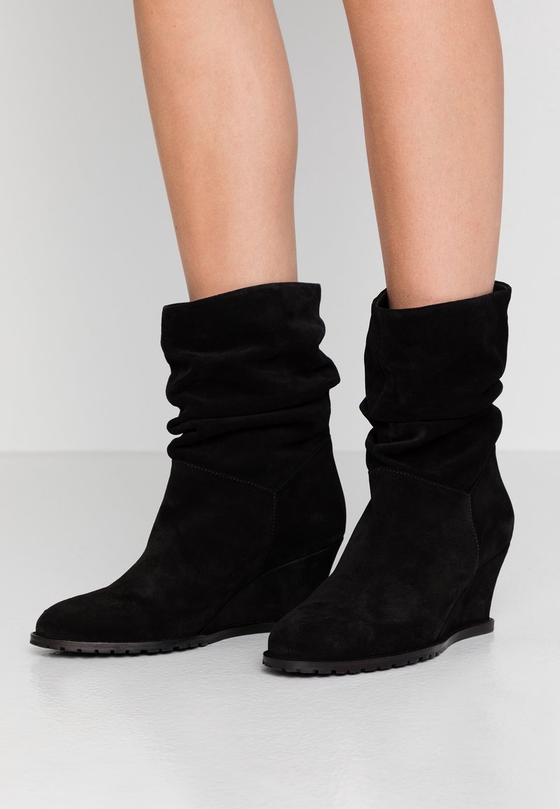 Bottines compensées en daim noir avec tige souple, bout pointu, surface texturée et semelle en caoutchouc pour une meilleure adhérence.