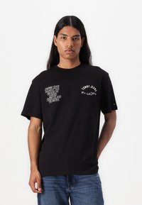 Sort bomulds t-shirt med hvide tekstgrafikker, herunder "Empire State," "Brooklyn," og "Tommy Jeans." Kortærmet og med rund hals.