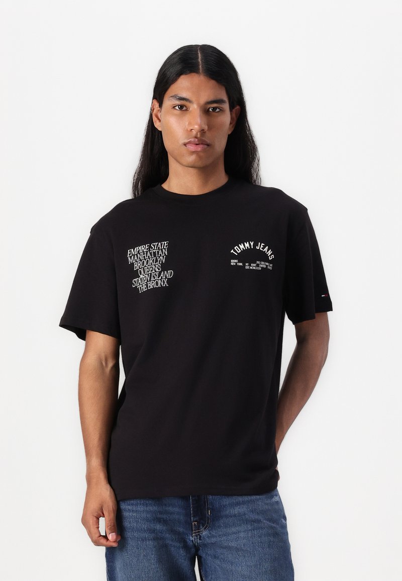 Camiseta de algodón negra con gráficos en texto blanco que incluyen "Empire State", "Brooklyn" y "Tommy Jeans". Diseño de manga corta y cuello redondo.