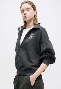 Donkergrijze ritscrewbewater met een hoge kraag, ribbelmanchetten en een geborduurd "PARIS" logo op de borst. Zacht materiaal met een relaxed fit.