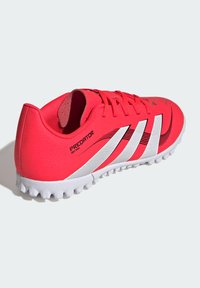 Scarpa da calcio rossa con strisce bianche, materiale superiore testurizzato, lacci piatti e suola in gomma modellata per trazione. Presenta il marchio "PREDATOR".