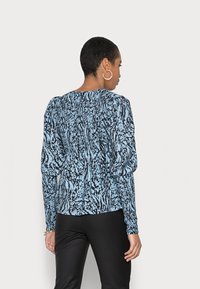 Blusa de manga longa puff com estampa abstracta azul e preta, com costas franzidas e decote redondo, combinada com calças pretas.