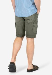 Olive green cargo shorts with multiple pockets, durable fabric, and a relaxed fit, paired with brown sandals and a blue striped shirt.