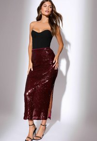 Kvinna i svart strapless topp och midiklänning i bordeaux med paljetter och sidslits, ihop med svarta klackskor med ankelsnörning.
