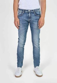 Jeans slim fit blu in denim, con tasche frontali, leggera scoloritura e cuciture a contrasto, abbinati a sneakers bianche.