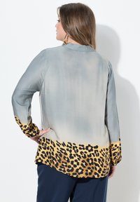 Silkebluse med en gradient fra lys grå til leopardprint i kant i guld og sort. Har lange ærmer og en subtil krave.