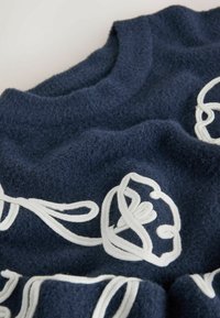 Marineblå sweater med en blød, struktureret finish. Indeholder hvide broderede blomsterdesigns og en rundet halsudskæring.