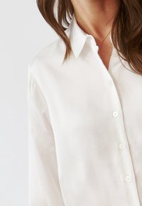 Vit skjorta med knapp-up i lätt material, med klassisk krage, långa ärmar och vita knappar fram.