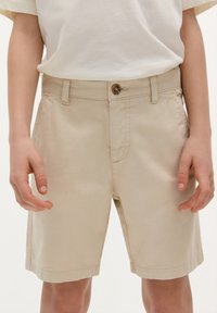 Pantaloni shorts beige con chiusura a bottone, passanti per cintura, tasche laterali, taglio dritto e tessuto di cotone morbido.