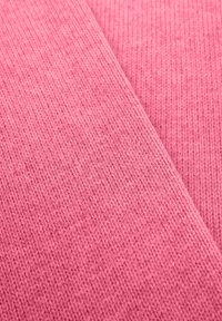 Roze gebreide stof met een geribbelde textuur, met twee overlappende delen. Het materiaal lijkt zacht en flexibel.