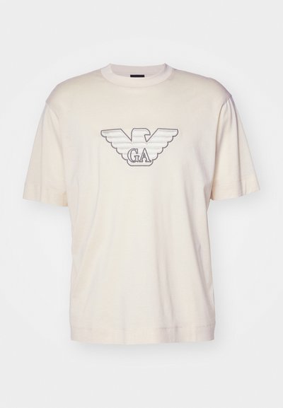 Šviesiai bežinė medvilninė marškinė, su dideliu siuvinėtų erelio logotipu pilkos ir juodos spalvos krūtinėje. Trumpomis rankovėmis, laisvu siluetu.