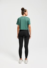 T-shirt de sport verte raccourcie à manches courtes, associé à un legging noir taille haute. Présente une texture lisse avec un logo au dos.