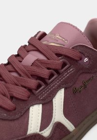 Κοντινό πλάνο ενός σκούρου μπορντό σουέντ αθλητικού παπουτσιού με μπορντό κορδόνια, λευκή πλευρική ρίγα και χρυσό λογότυπο "Pepe Jeans" στην πλευρά και τη γλώσσα.