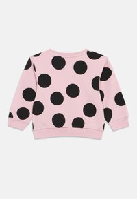 Sweatshirt rosa com grandes bolinhas pretas, punhos e barra canelados, e um decote redondo. Fabricado em uma mistura de algodão macio.