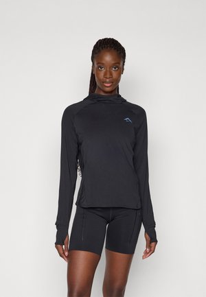 Tricou sportiv cu mânecă lungă de culoare neagră, dotat cu glugă, realizat dintr-un material ușor, având un mic logo albastru pe piept. Asortat cu pantaloni scurți negri.