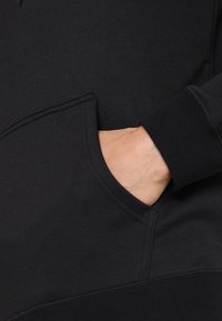 Felpa nera con tasca frontale e polsini a costine. Il tessuto sembra morbido e strutturato, progettato per comfort e calore.