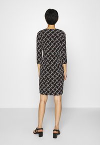 Robe noire à manches courtes avec un motif géométrique blanc et orange, réalisée en tissu lisse, avec une coupe ajustée tombant à mi-cuisse.