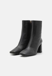 Botas de tobillo de cuero negro con tacón cuadrado, punta afilada y cremallera lateral. Textura suave y mínimo detalle de costura.