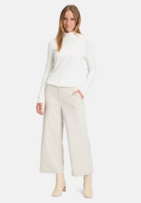 Fehér garbó pulóver széles szárú bézs nadrággal párosítva. Sima textúra, laza fazon és enyhe fényesség. A modellen bézs bokacsizma található.