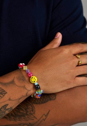 Farverig perlearmbånd med forskellige former, herunder et smilende ansigt, lavet af materialer som plastik og en fleksibel snor.