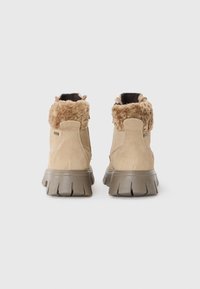 Bottines en suédine beige avec un col en fourrure beige et des semelles en caoutchouc épaisses dotées de rainures profondes pour une traction optimale. Deux languettes de tirage sur le dessus.