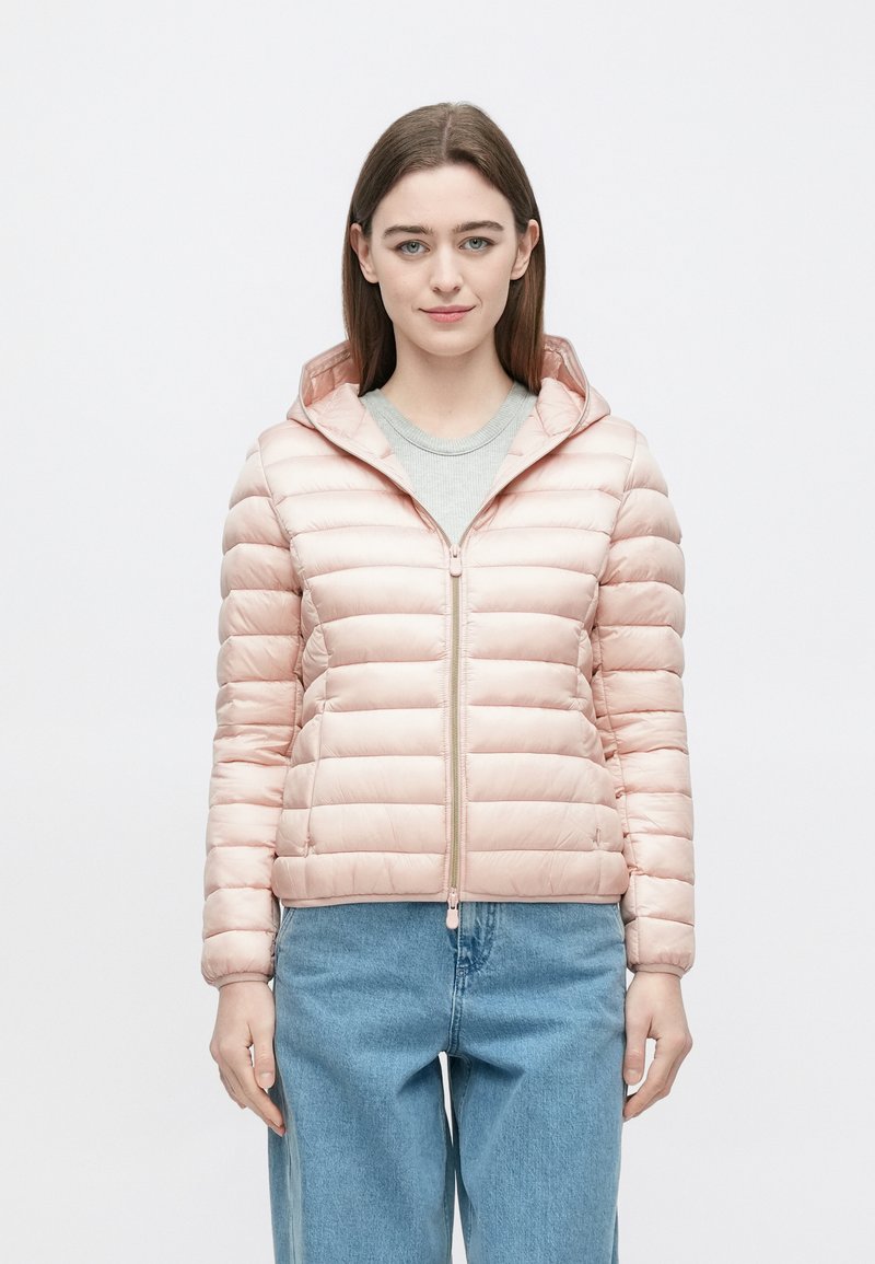 Polstret lyserød jakke med hætte, med lynlås foran og ribbet manchet. Båret over en lysegrå skjorte og kombineret med blå jeans.