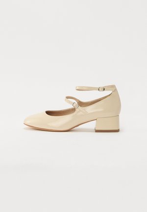 Scarpa Mary Jane in vernice beige con punta arrotondata e due cinturini alla caviglia regolabili. Presenta un tacco basso quadrato e una superficie liscia.